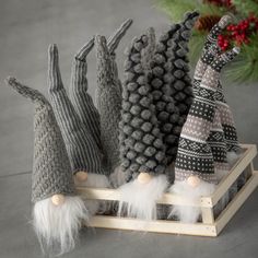 four knitted gnomes sitting on a sled with pine cones in the background