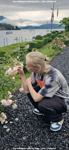 a woman kneeling down in front of flowers on the side of a road next to water