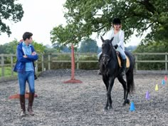 a woman riding on the back of a black horse next to a man in blue