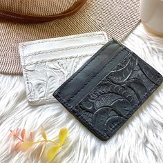 two leather wallets sitting next to each other on a white fur covered surface with flowers in the background