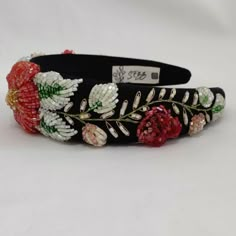 a black headband with red flowers and green leaves on the side, sitting on a white surface