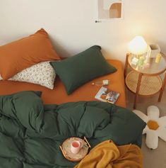 a bed with green sheets and pillows on it, next to a small side table