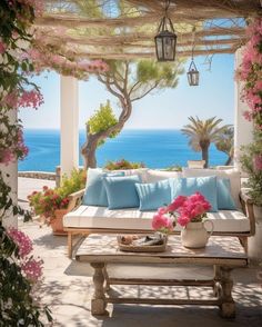 an outdoor seating area with blue and white pillows, pink flowers and potted plants