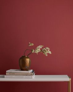 a gold vase with flowers on top of a white table next to a red wall