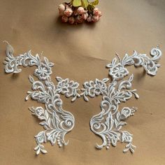 two pieces of white lace sitting on top of a brown surface next to some flowers