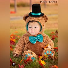 a baby in a teddy bear costume sitting on the grass with flowers and trees behind him