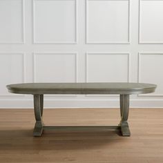 an oval dining table with wooden legs in front of a white wall and hardwood floor