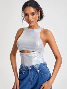 a woman wearing a silver crop top and denim shorts with her hands on her hips