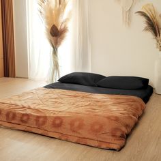 a bed sitting on top of a wooden floor next to a vase with dry grass