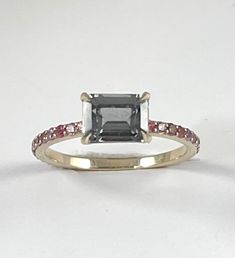 Cast in 18k white gold. A stunning gunmetal grey spinel gemstone faceted in a traditional emerald cut set in sharp stylized prongs. The band is cast in 18k white gold and features multi shade pink sapphire accent stones. - 18k white gold - .88ct emerald cut grey spinel - .33ctw pink purple sapphires Available in 18k white, 18k yellow and 18k rose gold inquire for platinum pricing. Most CM pieces can be made to order with alternate gemstones. Please inquire at cm@carlamorrison.com This Carla Morr Modern Emerald Cut Sapphire Ring With Accent Stones, Emerald Cut Sapphire Ring With Rose Cut Diamonds, Emerald Cut Ruby Ring With Rose Cut Diamonds, Emerald Cut Pink Sapphire Ring In Fine Jewelry Style, Fine Jewelry Emerald Cut Pink Sapphire Ring, Emerald Cut Pink Sapphire Ring, Spinel Gemstone, Pink Sapphire Ring, Purple Sapphire