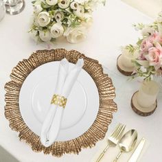 a table set with white and gold plates, silverware and flower centerpieces