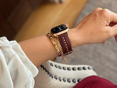 a woman wearing a watch and bracelet on her wrist with an apple watch in the background