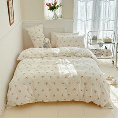 a white bed with pink flowers on it in a small room next to a window