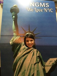 a woman standing in front of a sign with the statue of liberty on it