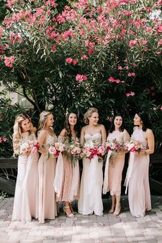 a group of women standing next to each other in front of trees with pink flowers