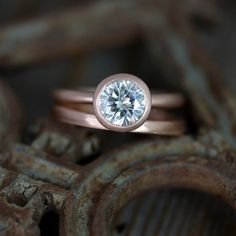 a rose gold engagement ring with a round brilliant diamond in the center, sitting on rusty metal