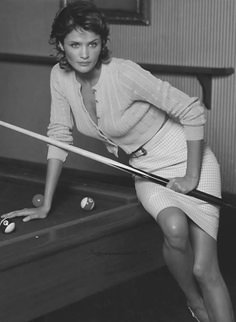 a woman leaning on a pool table with a cue in her hand and balls around her waist