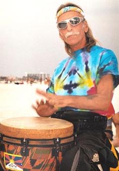 a man sitting on top of a drum in front of the ocean with sunglasses on