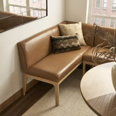 a corner couch with pillows on it in front of a mirror and table next to a window