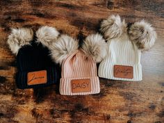 three hats with fur pom - poms on top of a wooden table next to each other