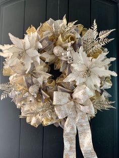 a wreath with white and gold flowers hanging from the front door on a black door