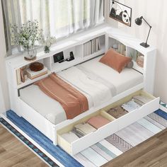 a white bed with drawers underneath it in a room next to a window and rug