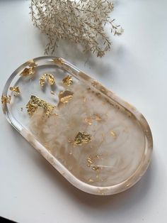 a tray with gold flecks on it next to a white flower and some dried plants