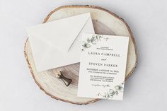 the wedding stationery is laid out on a wood slice with an envelope and ring