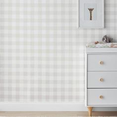 a baby's room with a white dresser and giraffe print on the wall