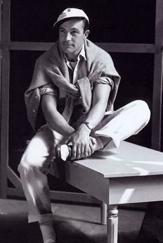 a man sitting on top of a wooden table next to a window in black and white