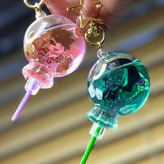 a person is holding two different colored glass keychains with charms attached to them