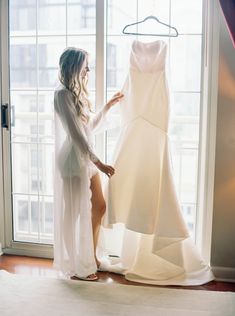 a woman standing in front of a window next to a white dress