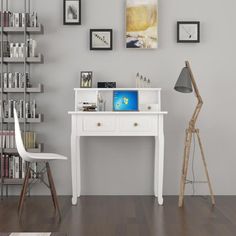 a white desk sitting in front of a book shelf filled with lots of books next to a lamp