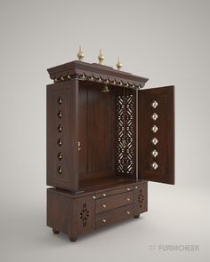 an ornate wooden cabinet with two doors open and gold knobs on the top, in front of a gray background