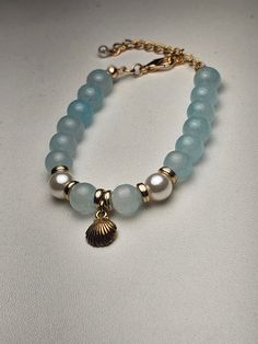 Dive into coastal elegance with our "Ocean Breeze Bracelet." This stunning piece features light blue beads intertwined with delicate gold accents, perfectly complemented by lustrous pearls that evoke the serenity of the sea. The centerpiece is a beautiful shell pendant, adding a touch of beachy charm to the design. Whether you're dressing up for a special occasion or adding a touch of oceanic beauty to your everyday look, this bracelet is sure to make a statement. Handcrafted with care, it's a perfect gift for someone special or a lovely treat for yourself. - Materials : Light blue beads, gold accents, pearls, shell pendant - Length : 6 inches Embrace the essence of the sea with this elegant bracelet that effortlessly captures the beauty of the ocean. Beach Jewelry With 8mm Blue Beads, Blue 8mm Bead Jewelry For The Beach, Blue Beaded Jewelry For Beach, Blue Beaded Jewelry For The Beach, Blue Beaded Bracelet With Pearl Charm As Gift, Blue Beaded Bracelet With Pearl Charm For Gift, Blue Jewelry With Pearl Charm And Round Beads, Elegant Blue Beaded Bracelets With Pearl Charm, Elegant Blue Beaded Bracelet With Pearl Charm