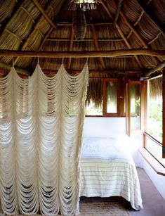 a bed sitting under a wooden roof next to a window covered in white sheer curtains