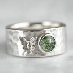 a close up of a ring with a butterfly on the side and a green stone in the middle