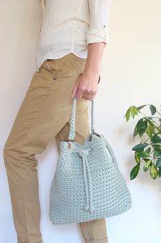 a woman is holding a crocheted purse in front of a potted plant