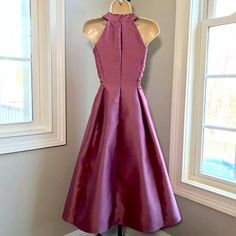 a purple dress on a mannequin stand in front of a window with the sun shining