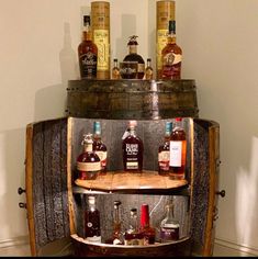 an old wooden barrel with liquor bottles on the top and bottom shelves, in front of a white wall