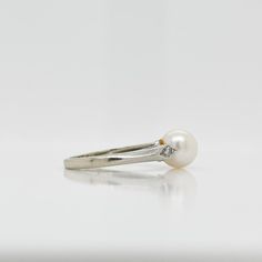 A fine Retro signed pearl cocktail ring.  In 14k white gold.  Set with 7mm round white pearl and flanked by two small accent diamonds on the shoulder of the setting.  Marked to the shank for Rothman & Schneider of New York City.  Simply a wonderful Mid-Century ring!  Date: Mid-20th Century  Overall Condition: It is in overall good, as-pictured, used estate condition with some fine & light surface scratches and other signs of expected light wear consistent with age.  Fineness: Marked 14k for gold Timeless White Gold Pearl Ring With Diamond Accents, White Pearl Rings With Diamond Accents, White Gold Pearl Ring With Diamond Accents For Promise, Classic White Pearl Ring With Diamond Accents, Classic Akoya Pearl Rings With Diamond Accents, Timeless White Gold Pearl Ring With Center Stone, Classic White Gold Pearl Diamond Ring, Classic White Gold Pearl Drop Ring, Classic Pearl Diamond Ring With Accents