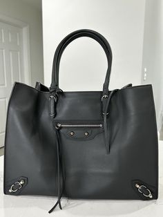 Used, Like New Balenciaga Papier A4 Zip Around Classic Studs Bag Leather Large - hard to find gray color. HUGE size, great for daily use (work, travel, etc). Beautiful condition, only used a few times. Balenciaga Papier A4 Zip Around Classic Studs Bag Leather Large. Purchased from Balenciaga boutique as a work/travel bag and only used it about 3x. Great size for work, travel, baby/kids, etc. Beautiful leather and unique color (the shade was always complimented when wearing). Working remotely and don't need as many totes for daily transporting, only reason I'm selling this item as it deserves a good home! Brand Code: 357331.1000.C.1669 SIZE AND FIT: 15.5"W x 12"H x 6.5"D, 8" handle drop Exterior Color: Dark Grey Interior Color: Dark Grey Exterior Material: Leather Interior Material: Leather Work Travel Bag, Studded Bag, Grey Exterior, Silver Accessories, Leather Interior, Travel Bag, Colorful Interiors, Bags Handbags, Balenciaga