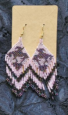 pink and black beaded earrings sitting on top of a piece of fabric