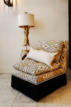 a gold and black chair sitting next to a lamp on top of a white tiled floor