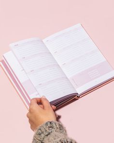 a person holding an open book in their left hand on a pink background with the pages lined up