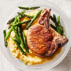 a white plate topped with meat and asparagus on top of mashed potatoes