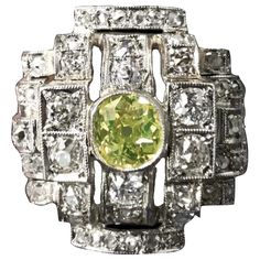 How do you like this lime-colored diamond engagement or cocktail ring? One-of-a-kind Art Deco Geometric Ring in Platinum and 19.2 Karat White Gold, featuring a Certified Natural Fancy Greenish Yellow Old Mine-cut diamond, Portuguese, late 1930s. The Fancy colored diamond with a hue that hints both green and yellow is millegrain-set to the center, amidst a sea of rectangular, squared and half-barrel plaques similarly-set throughout with 54 colorless and near colorless Old Mine-cut, Old European b Vintage Green Diamond Platinum Ring, Vintage Green Diamond Ring In Platinum, Art Deco Green Jewelry With Brilliant Cut, Vintage Green Diamond Ring With Center Stone, Green Art Deco Ring With Round Cut, Green Round Cut Art Deco Ring, Green Diamond Art Deco Rings, Art Deco Green Diamond Ring With Prong Setting, Art Deco Green Ring With Prong Setting