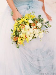 a woman in a blue dress holding a bouquet of yellow and white flowers on her wedding day