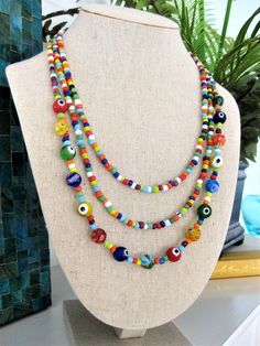 "I made this fun and colorful beaded necklace, with multi strands of glass seed beads, in a rainbow of colors. The larger glass beads on the longest strand, are made with multi colored evil eye beads, and multi colored millefiori beads. This necklace has 3 strands of colorful beads. Add color and get noticed, with this statement necklace for women who are fun and colorful. This colorful necklace is 24 inches long, and has a 2\" extension chain. This necklace is ready to send to you today, and in Multicolor Double Strand Beaded Necklace With Large Beads, Adjustable Multicolor Double Strand Beaded Necklaces, Handmade Multicolor Double Strand Beads, Multicolor Double Strand Necklace With Large Beads, Multicolor Double Strand Beaded Necklace For Beach, Handmade Multicolor Multi-strand Beads, Multicolor Round Beads Fun Necklace, Colorful Vibrant Beaded Necklace With Round Beads, Vibrant Multicolor Beaded Necklaces With Round Beads