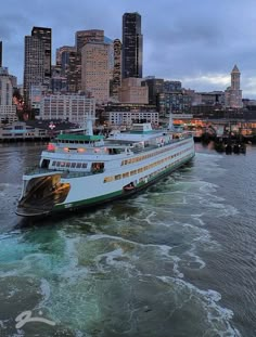 a large boat traveling down a river next to a tall cityscape at dusk